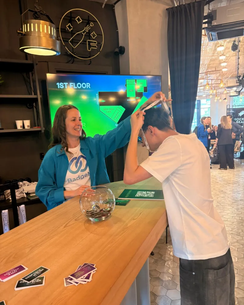 Staff member placing a BadgeMe lanyard over an attendee at the Deep Tech Atelier 2026 check-in desk